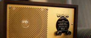 A virginia voice radio is pictured. It is a small, square, brown radio with gold plating on the front. It has a speaker on the left, and tuning knobs on the right.