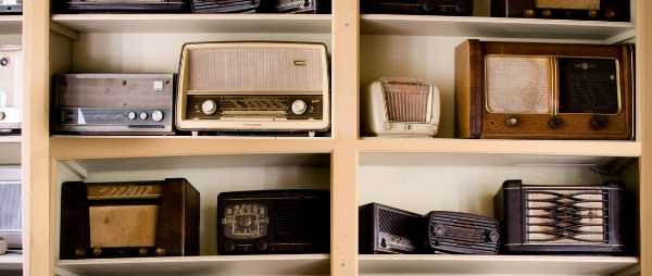 A shelf filled with radios is pictured. The radios are many different makes and models, from various time periods.